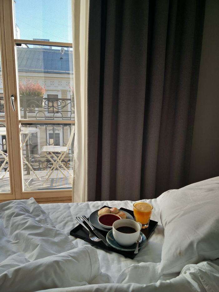 A relaxing breakfast tray with coffee and juice on a bed by a window overlooking the city.