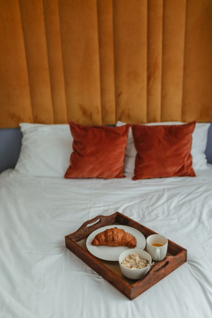 Cozy breakfast setup with croissant and coffee on a wooden tray in a bed setting.