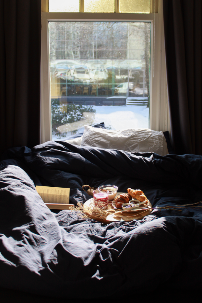 A cozy breakfast in bed featuring croissants and a book by a sunlit window.